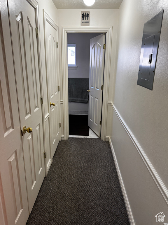 Hall featuring electric panel, baseboards, a textured ceiling, and dark carpet