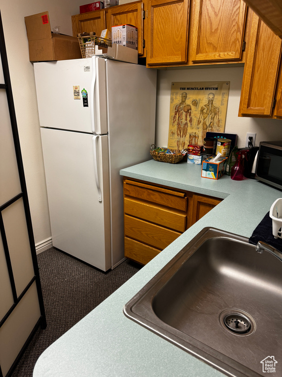 Kitchen with brown cabinets, a sink, stainless steel microwave, freestanding refrigerator, and light countertops