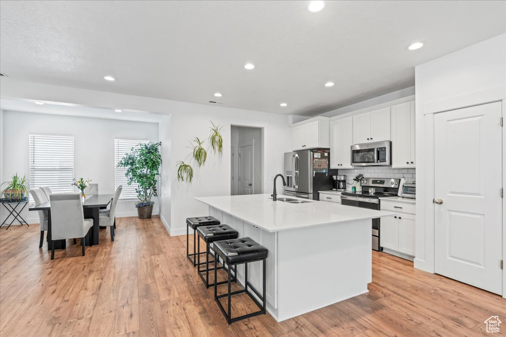 Kitchen featuring stainless steel appliances, a sink, a center island with sink, a breakfast bar area, and white cabinetry