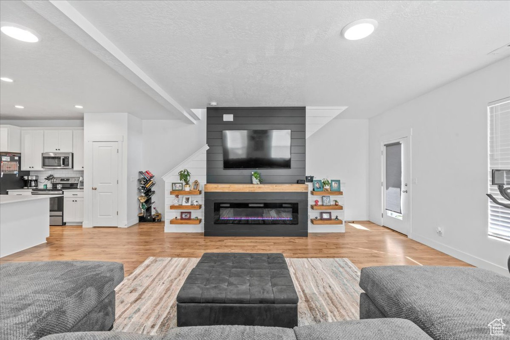 Living area with a glass covered fireplace, light wood finished floors, recessed lighting, and baseboards