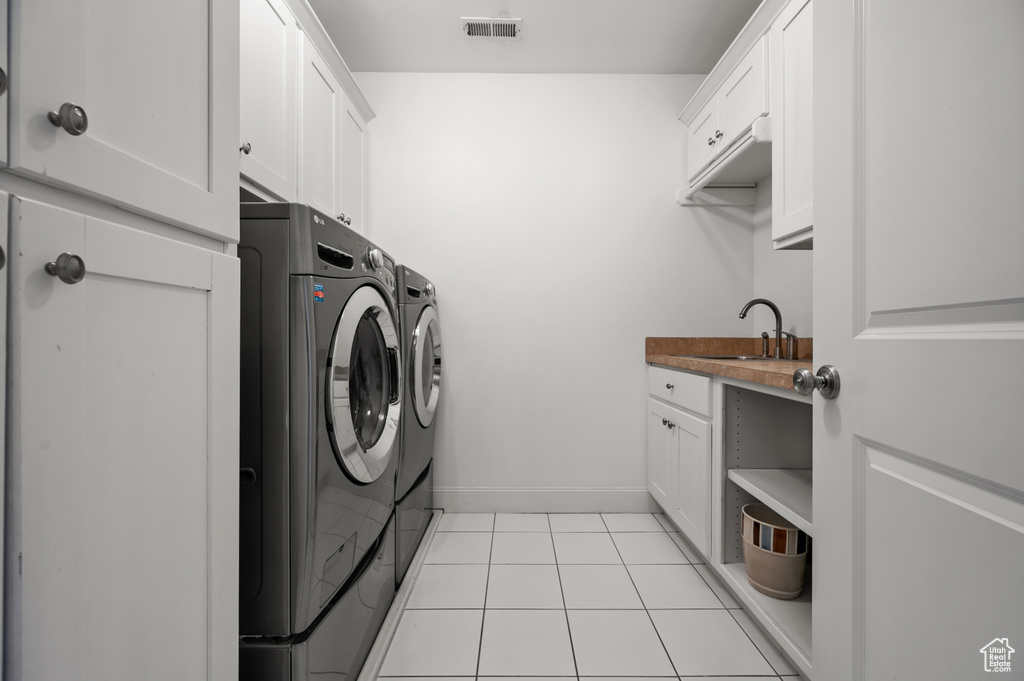 Laundry room with visible vents, light tile patterned floors, cabinet space, independent washer and dryer, and a sink