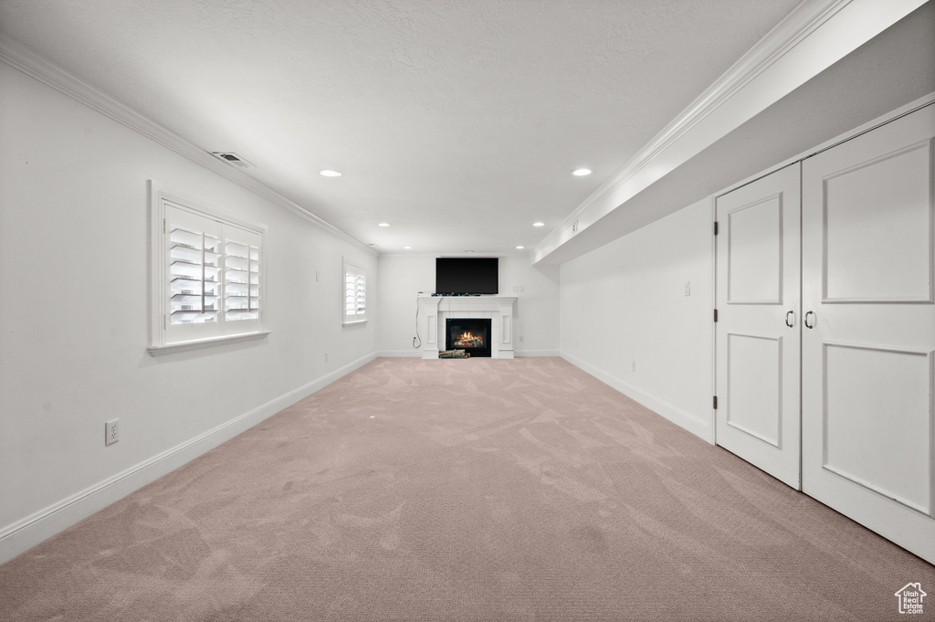 Unfurnished living room featuring crown molding, light colored carpet, visible vents, and baseboards