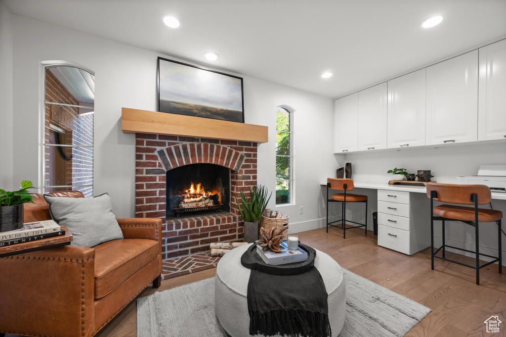 Living area featuring a brick fireplace, baseboards, recessed lighting, light wood-style flooring, and built in study area