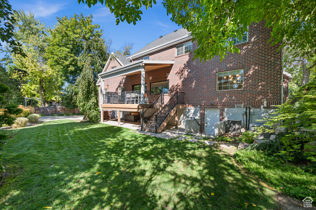 Rear view of house featuring a deck, stairway, a lawn, and brick siding