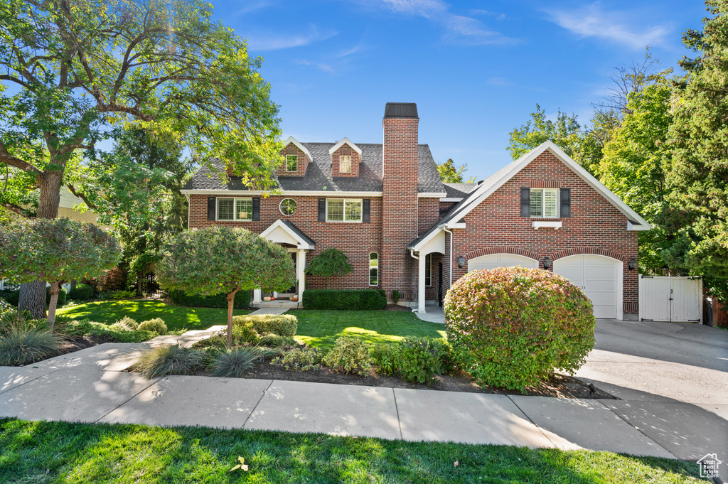 Colonial house featuring a front yard, fence, driveway, a chimney, and brick siding