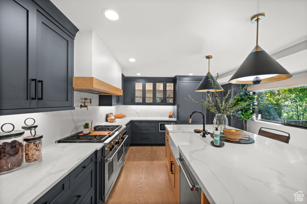 Kitchen featuring light stone counters, a sink, stainless steel appliances, custom range hood, and light wood-style floors