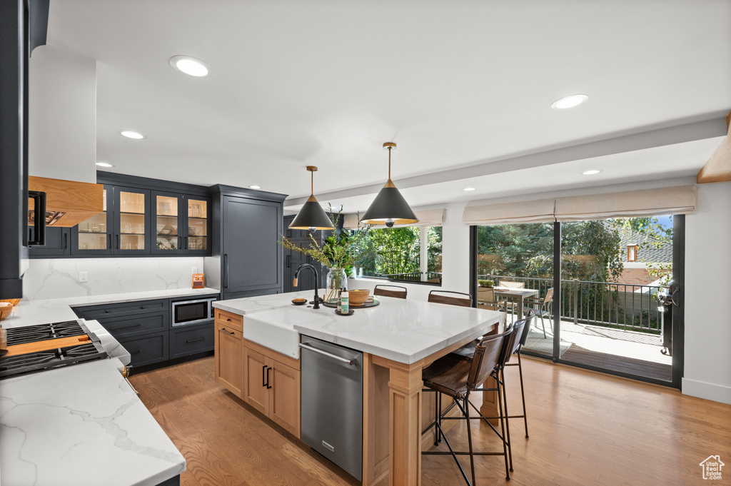 Kitchen featuring light stone countertops, a sink, glass insert cabinets, light wood-style floors, and appliances with stainless steel finishes