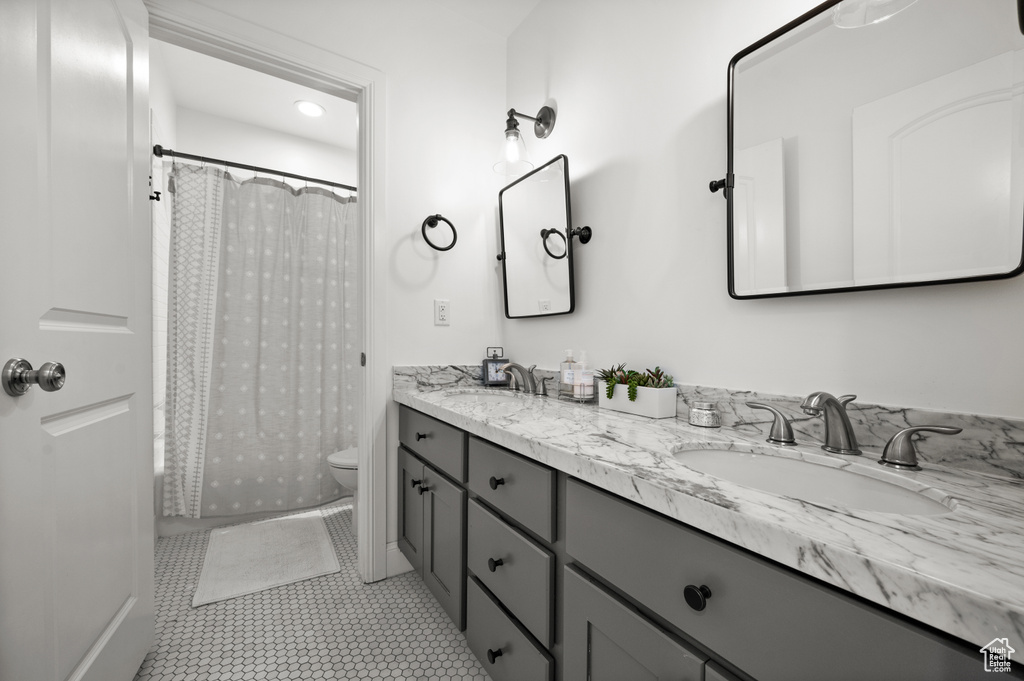 Full bathroom with double vanity, tile patterned flooring, toilet, and a sink