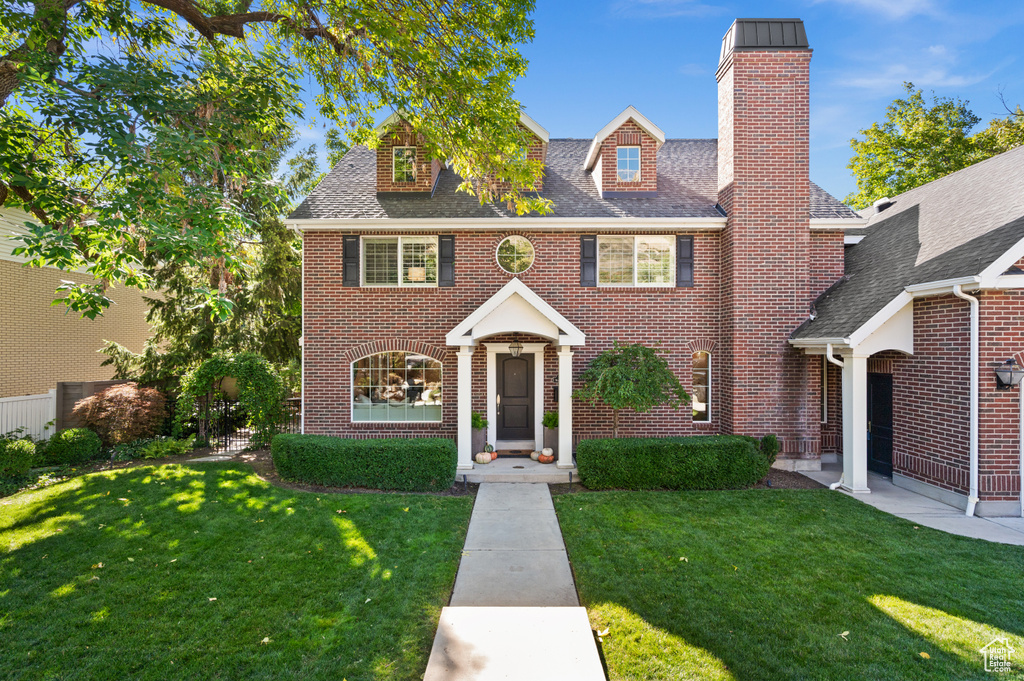 Georgian-style home with a front yard, brick siding, and roof with shingles