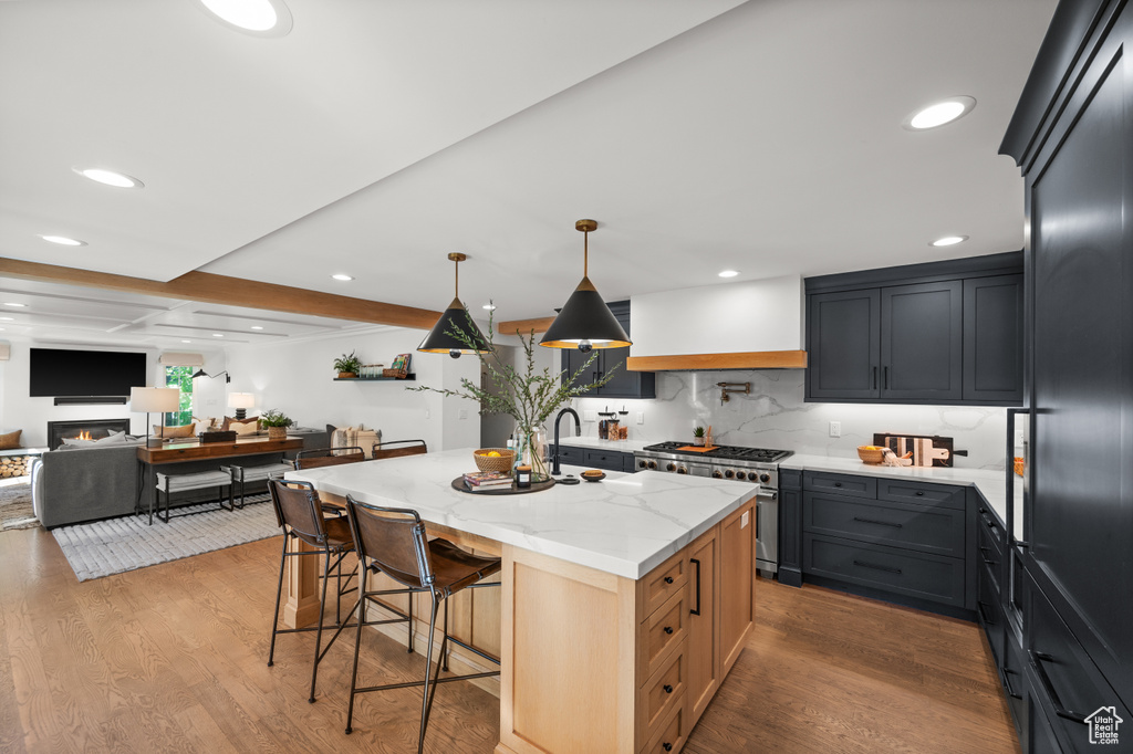 Kitchen with light stone counters, high end appliances, wood finished floors, a kitchen bar, and beamed ceiling