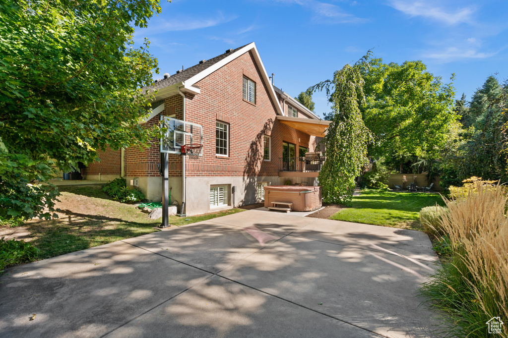 Back of property featuring brick siding, a hot tub, and a yard