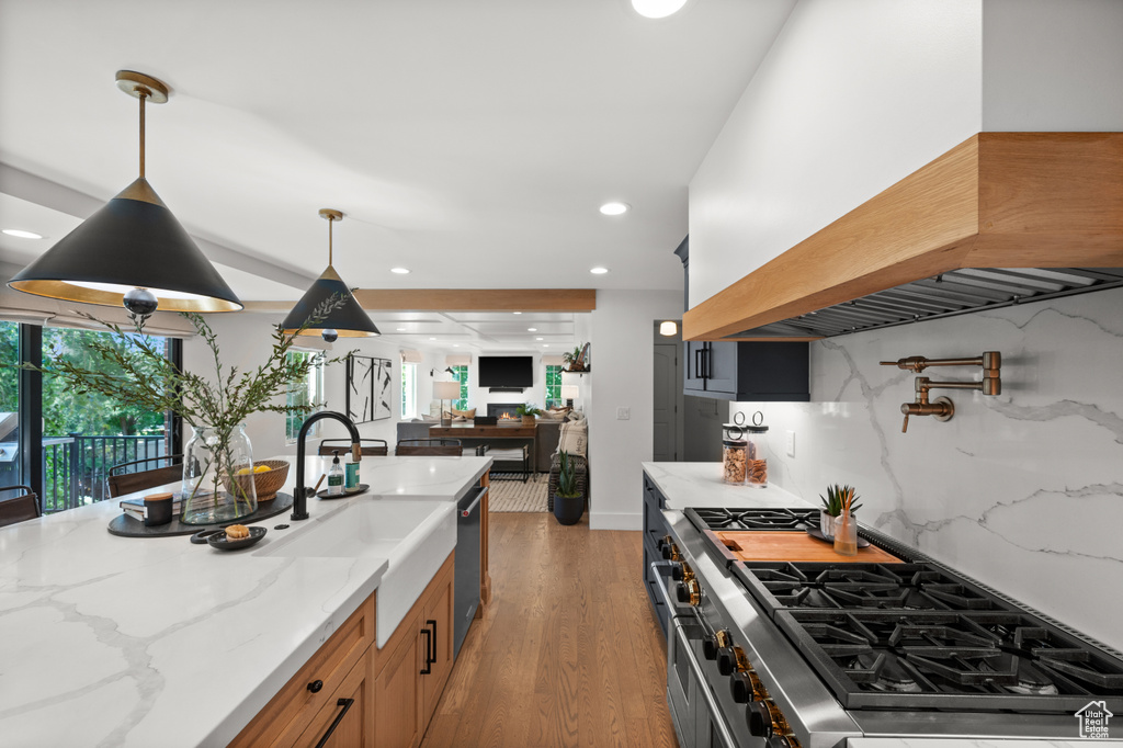 Kitchen featuring light stone counters, pendant lighting, wood finished floors, and custom range hood