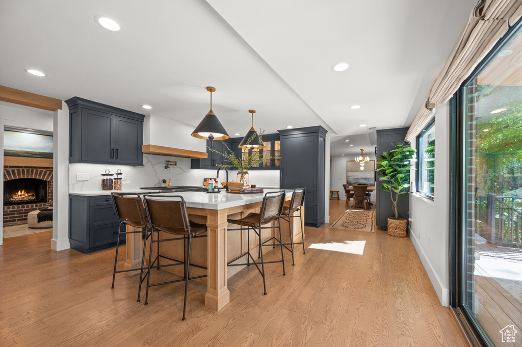 Kitchen featuring light wood finished floors, backsplash, light countertops, a kitchen breakfast bar, and custom exhaust hood