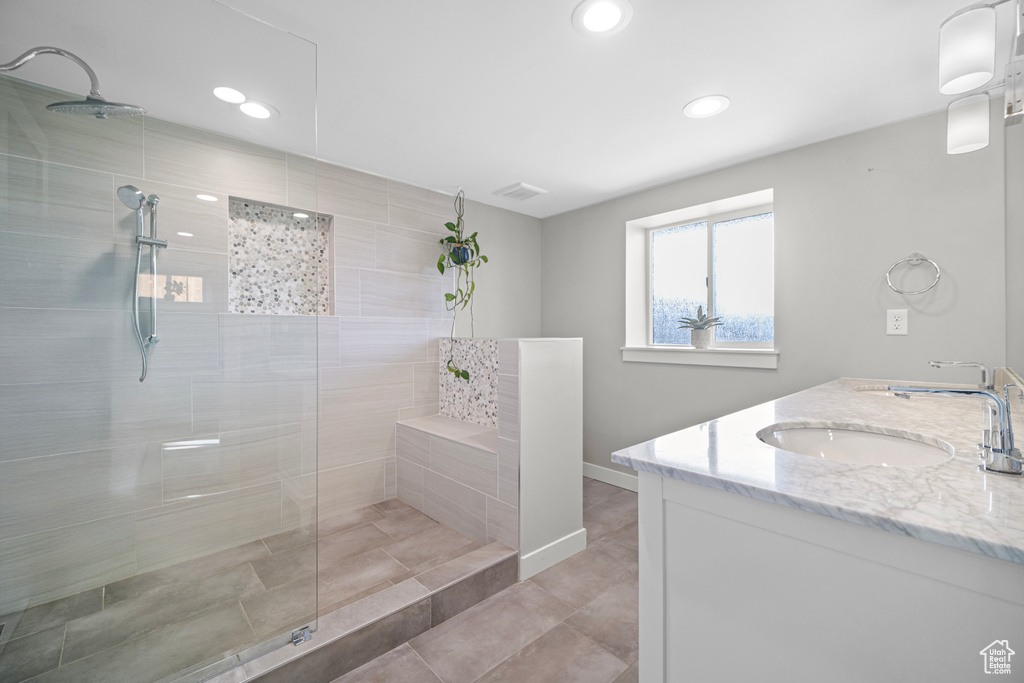 Bathroom featuring visible vents, baseboards, walk in shower, double vanity, and a sink