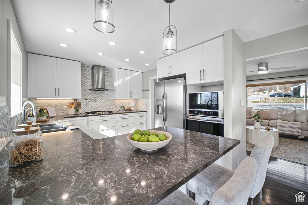 Kitchen with a sink, tasteful backsplash, dark wood-style floors, stainless steel appliances, and wall chimney exhaust hood