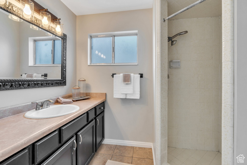 Full bath with a tile shower, tile patterned flooring, vanity, and baseboards