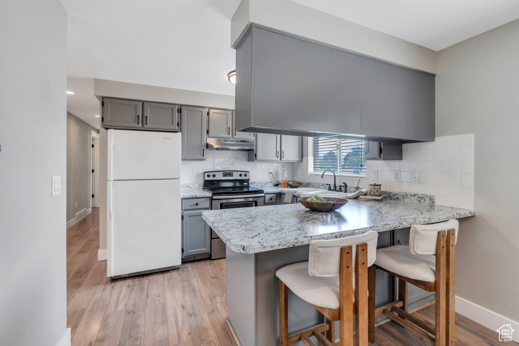 Kitchen with freestanding refrigerator, stainless steel electric range, under cabinet range hood, gray cabinetry, and a peninsula