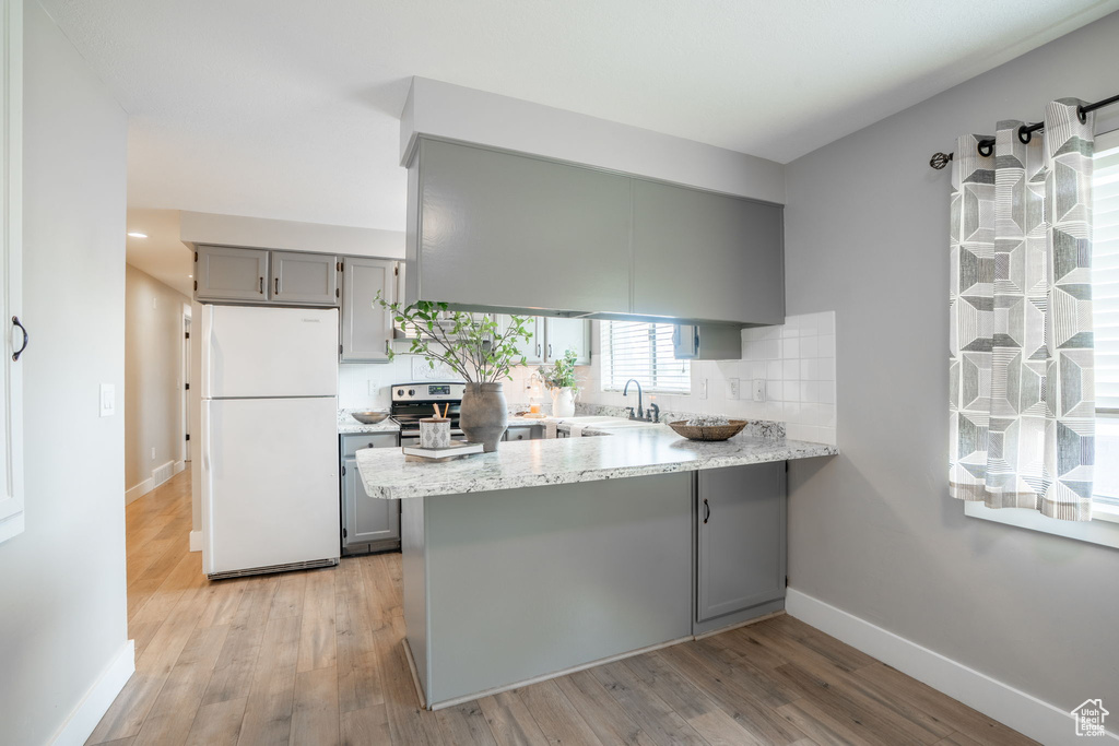 Kitchen featuring a sink, gray cabinets, freestanding refrigerator, a peninsula, and light wood-type flooring