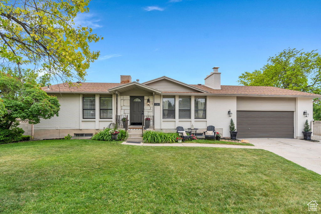 Single story home featuring a garage, concrete driveway, a chimney, a front yard, and brick siding