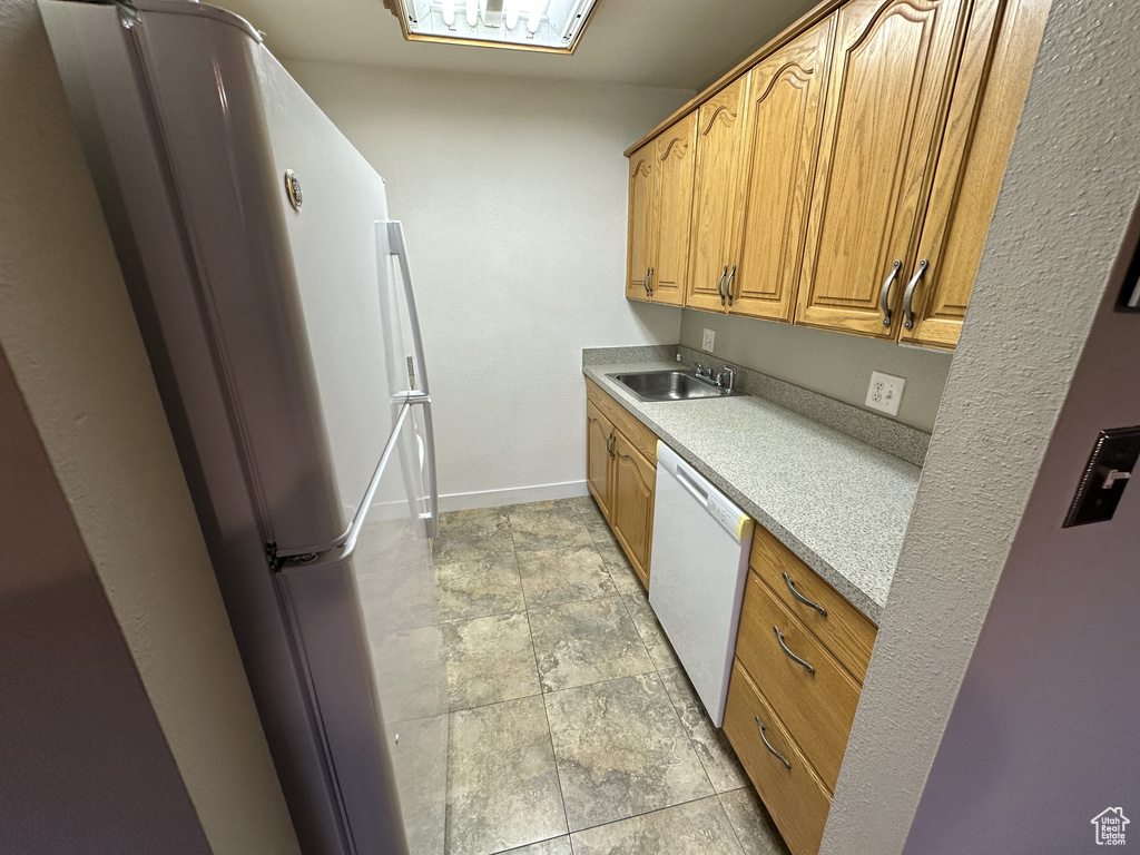 Kitchen with white appliances, light countertops, brown cabinetry, and light stone finish floors