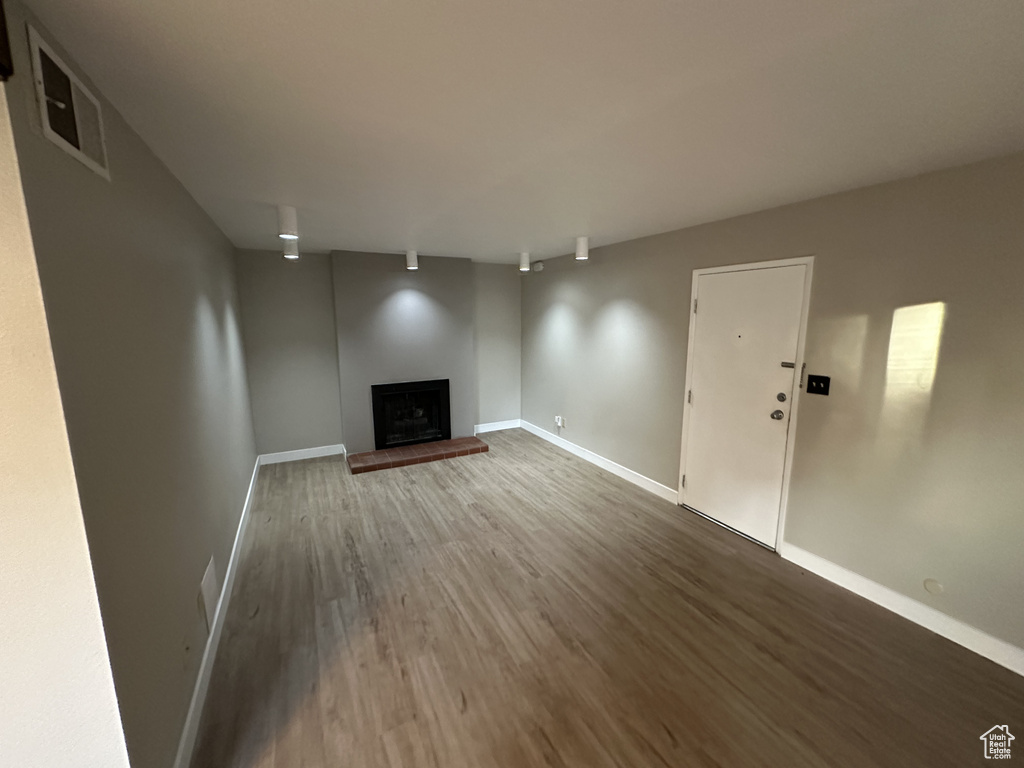 Unfurnished living room featuring a fireplace with raised hearth and wood finished floors
