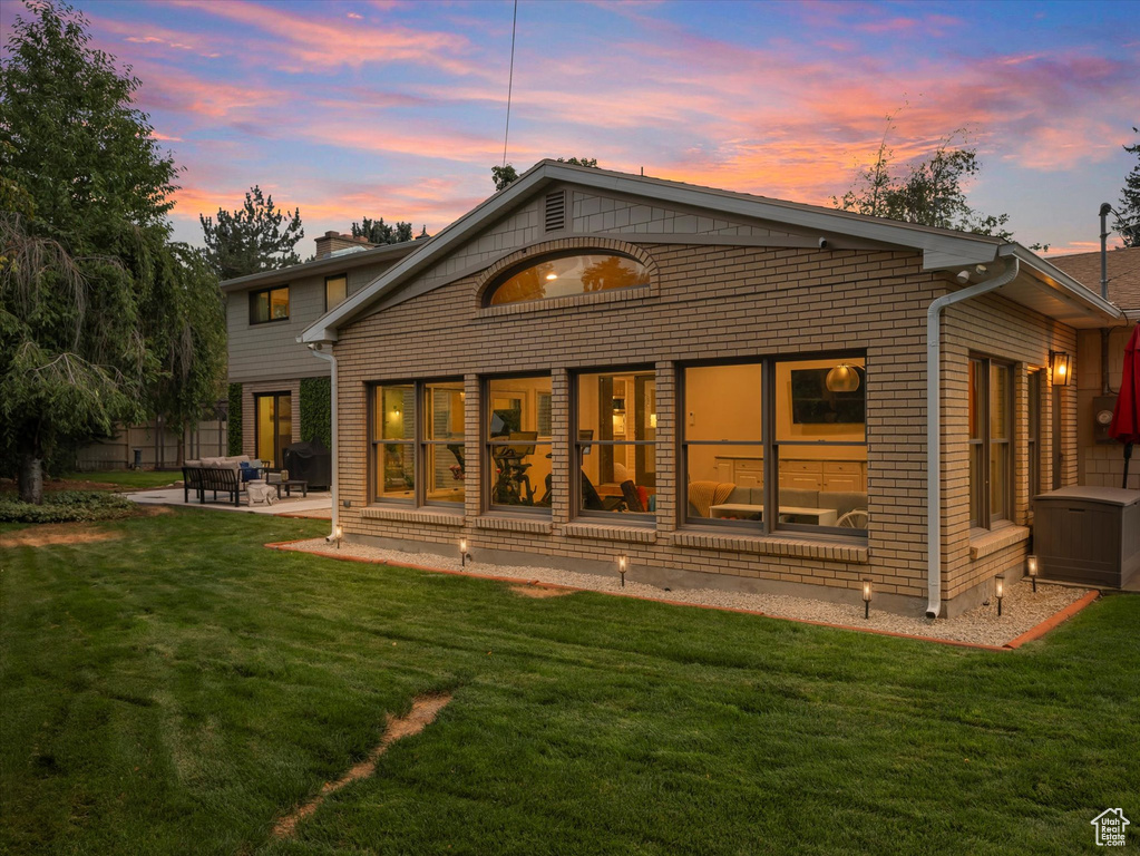 Back house at dusk featuring a patio area and a lawn