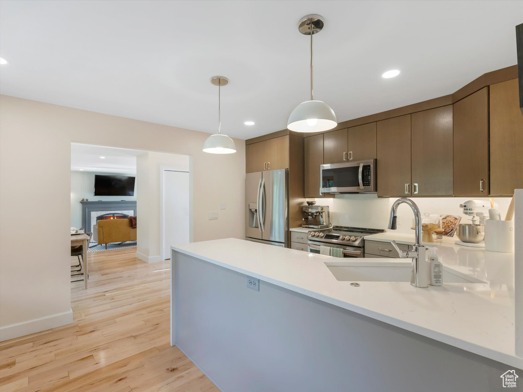 Kitchen with pendant lighting, sink, light hardwood / wood-style flooring, kitchen peninsula, and stainless steel appliances