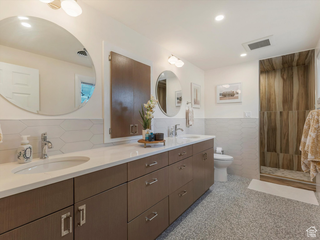 Bathroom with vanity, toilet, tile walls, and a tile shower