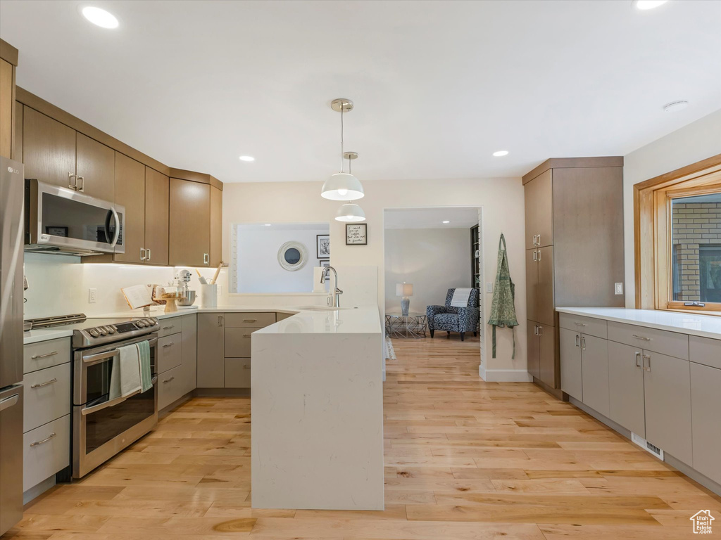 Kitchen featuring sink, light wood-type flooring, stainless steel appliances, and hanging light fixtures