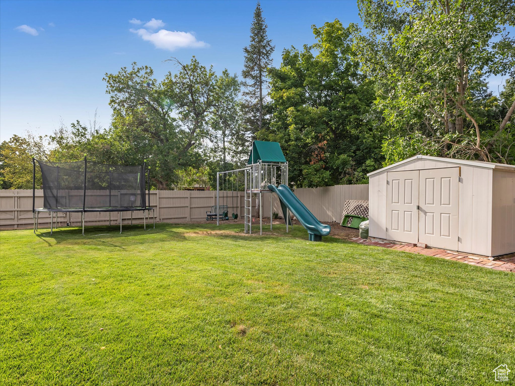 View of yard with a playground, a storage unit, and a trampoline