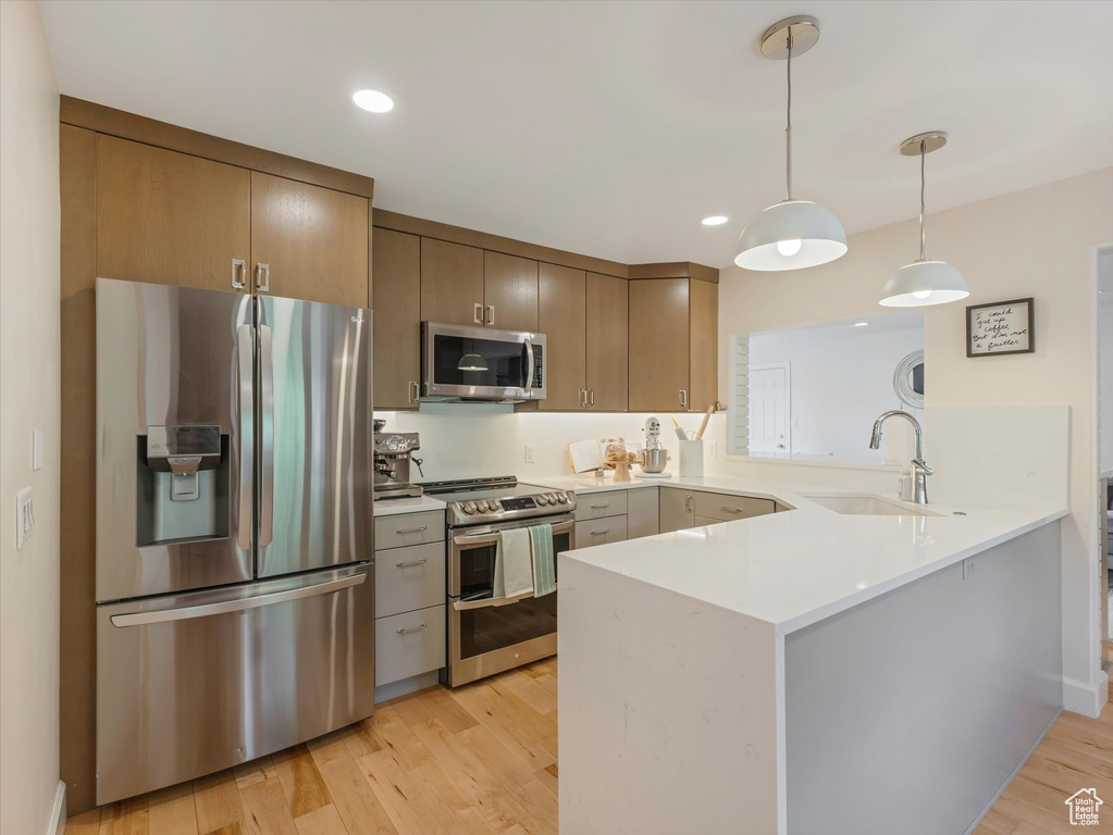 Kitchen featuring kitchen peninsula, appliances with stainless steel finishes, sink, decorative light fixtures, and light hardwood / wood-style flooring