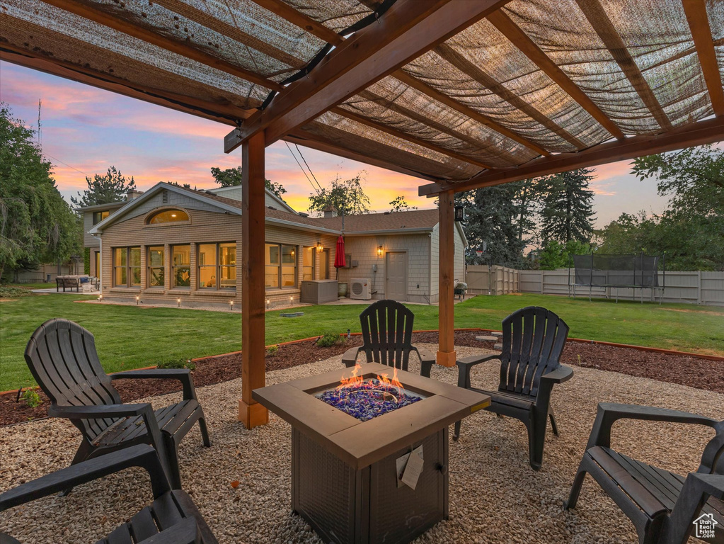 Patio terrace at dusk with a fire pit, a pergola, a trampoline, and a lawn