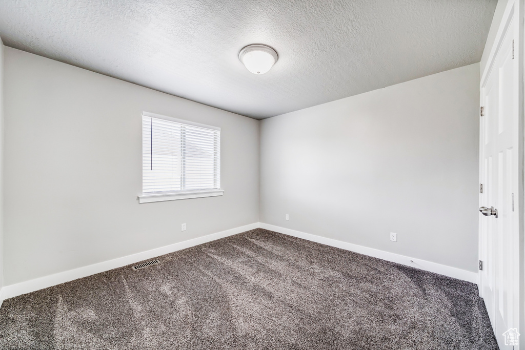 Carpeted spare room featuring baseboards, visible vents, and a textured ceiling