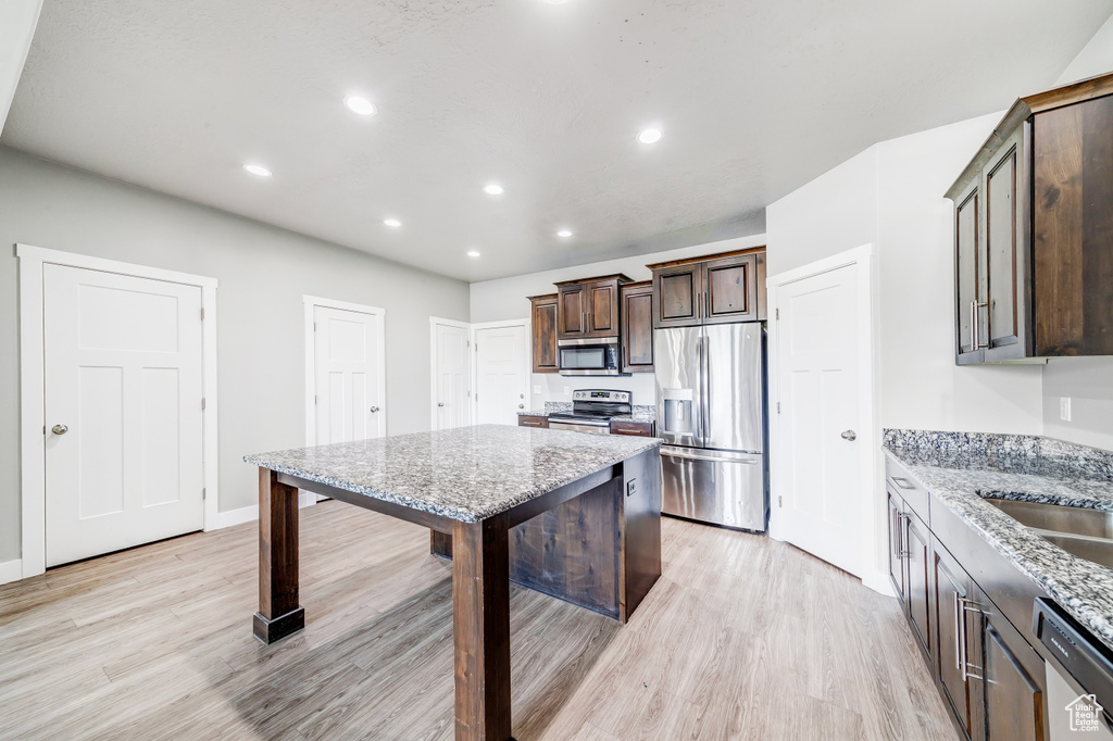 Kitchen with light wood-style flooring, light stone counters, stainless steel appliances, dark brown cabinets, and recessed lighting