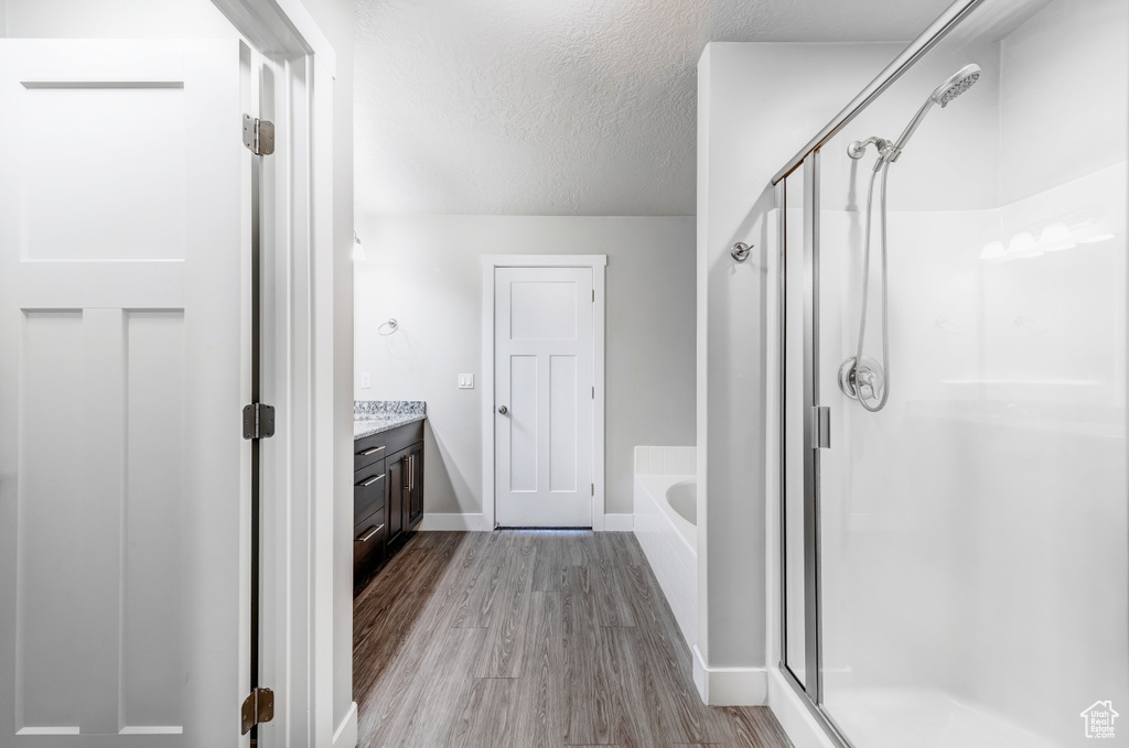 Bathroom with a bath, a stall shower, a textured ceiling, and wood finished floors