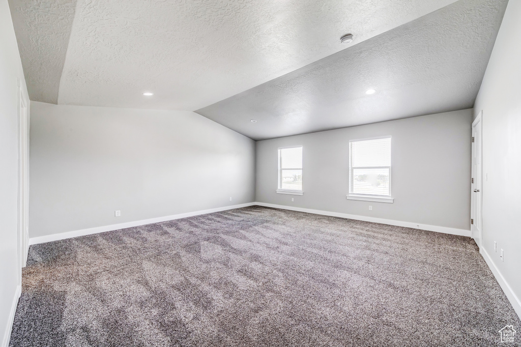 Unfurnished room featuring lofted ceiling, a textured ceiling, baseboards, and carpet flooring