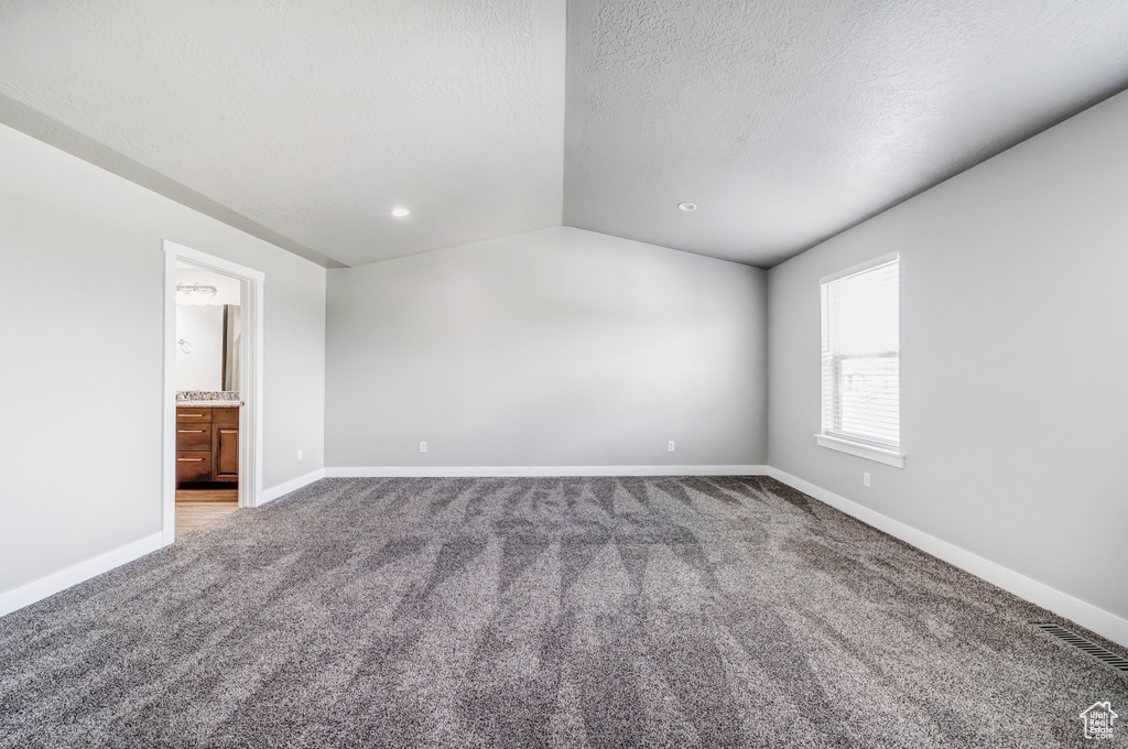 Carpeted spare room featuring baseboards, vaulted ceiling, a textured ceiling, and recessed lighting