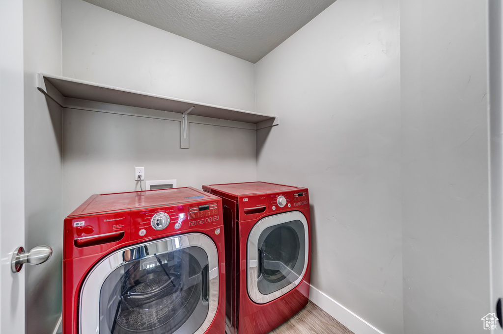 Washroom featuring a textured ceiling, separate washer and dryer, wood finished floors, laundry area, and baseboards