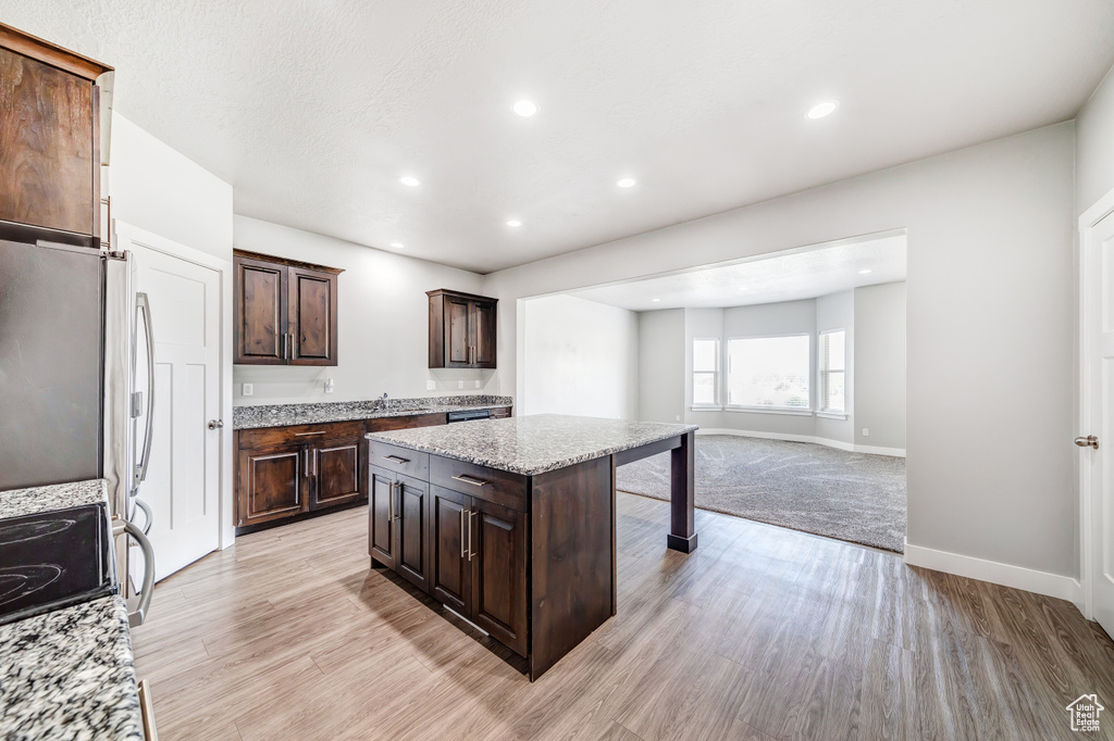 Kitchen with dark brown cabinetry, recessed lighting, a center island, light stone countertops, and light wood finished floors