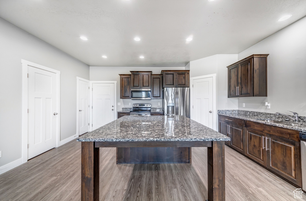 Kitchen featuring dark brown cabinetry, dark stone countertops, appliances with stainless steel finishes, and a sink