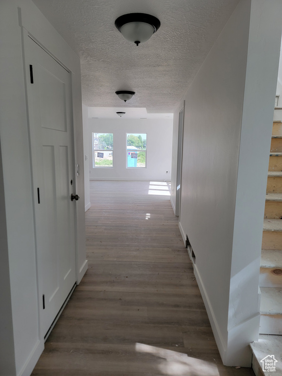 Corridor featuring a textured ceiling, stairway, baseboards, and wood finished floors