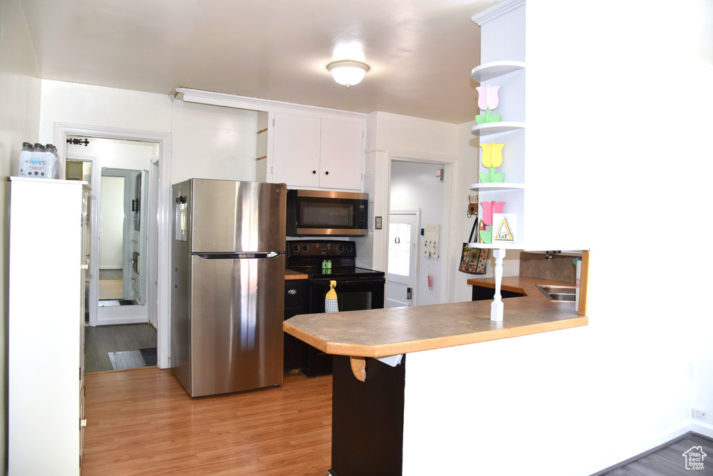 Kitchen with open shelves, light wood-style flooring, a peninsula, stainless steel appliances, and white cabinets