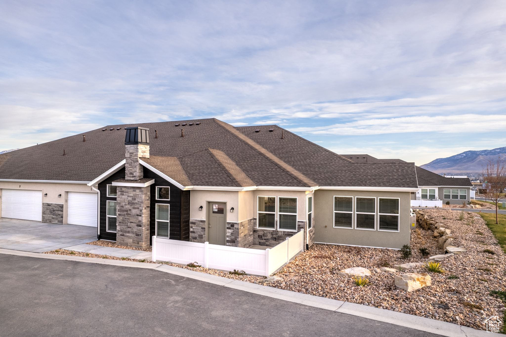 View of front facade with fence, roof with shingles, stucco siding, stone siding, and driveway