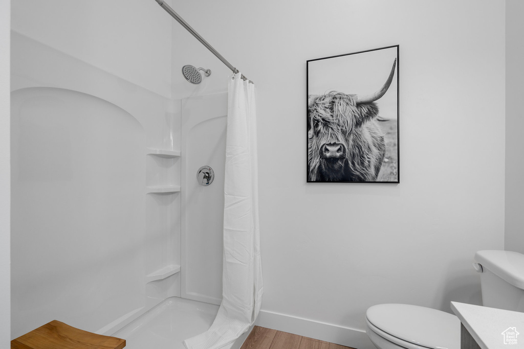 Full bath with curtained shower, toilet, wood finished floors, and baseboards