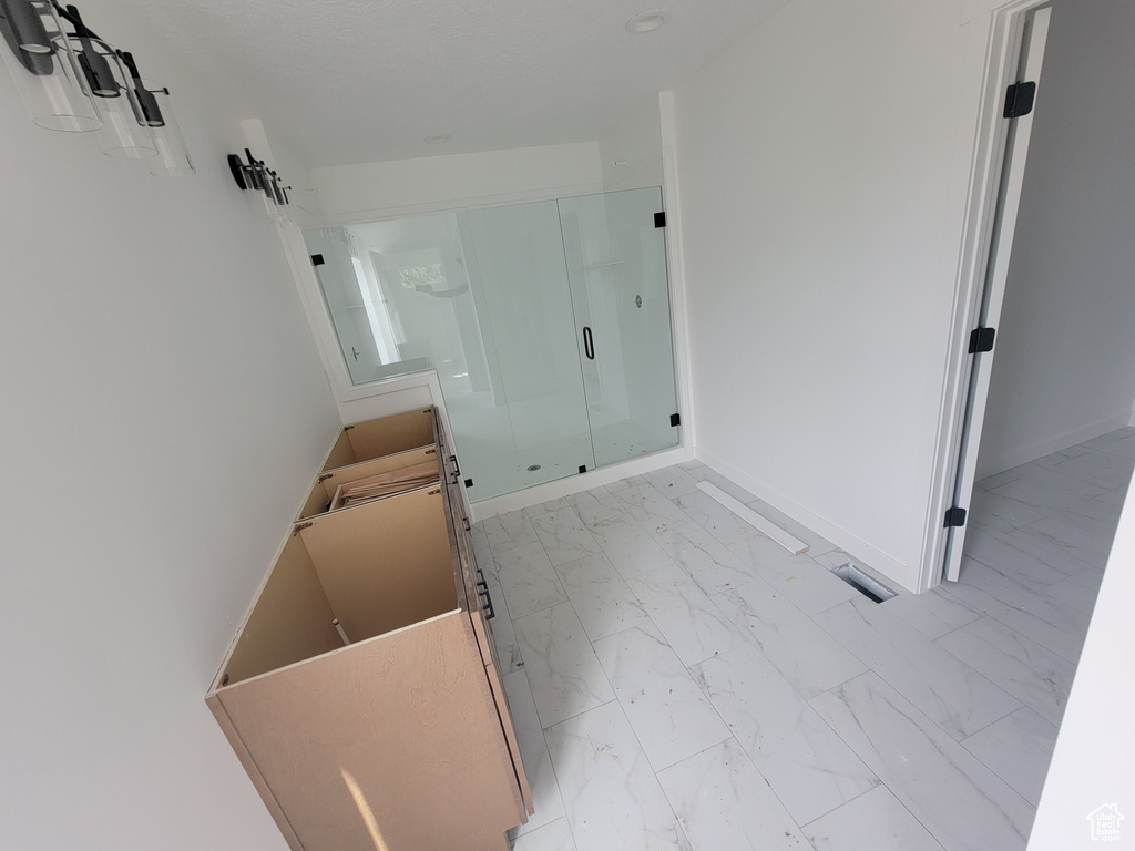 Full bathroom with marble look tile flooring, a shower stall, and baseboards