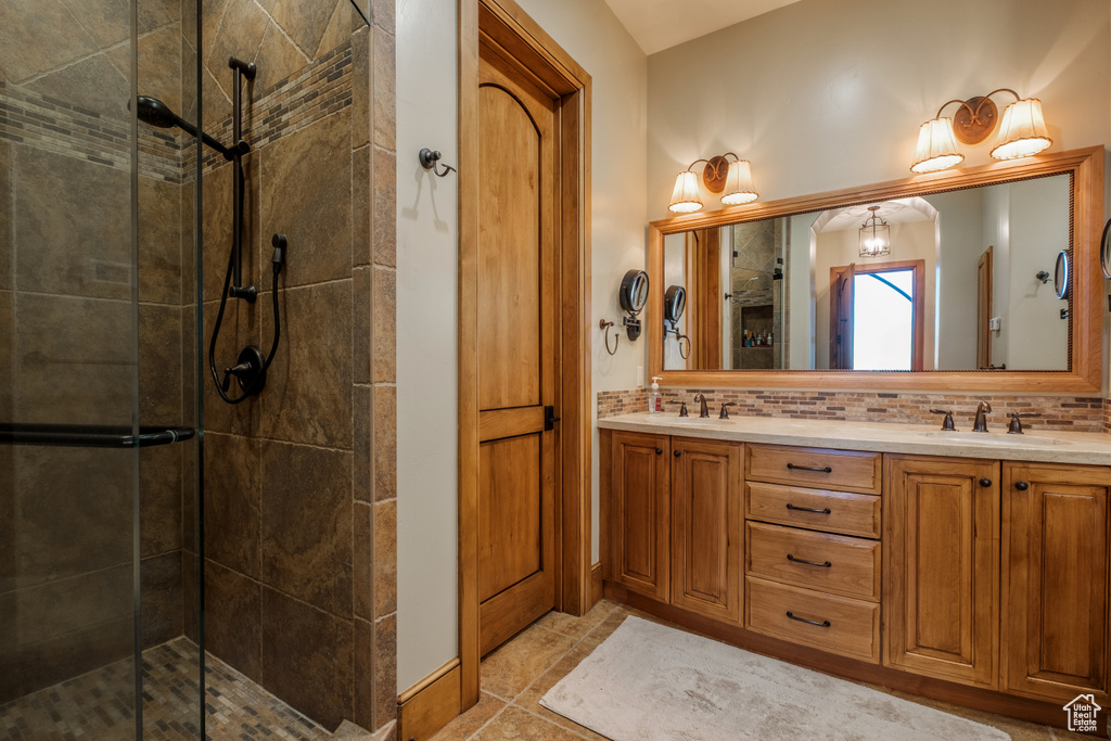 Full bath featuring a shower stall, double vanity, tasteful backsplash, and tile patterned floors
