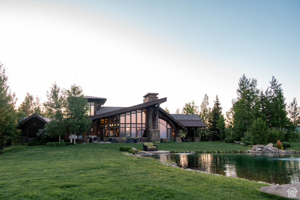 Back of property at dusk featuring a yard and a water view