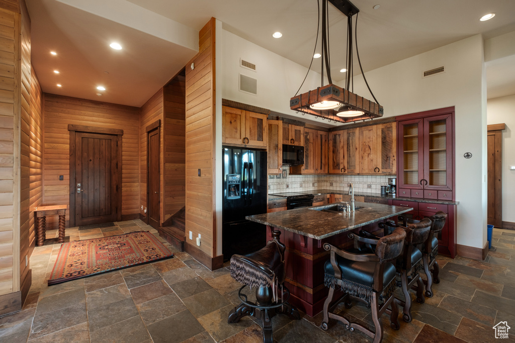 Kitchen with black appliances, stone tile flooring, a kitchen breakfast bar, tasteful backsplash, and a kitchen island with sink