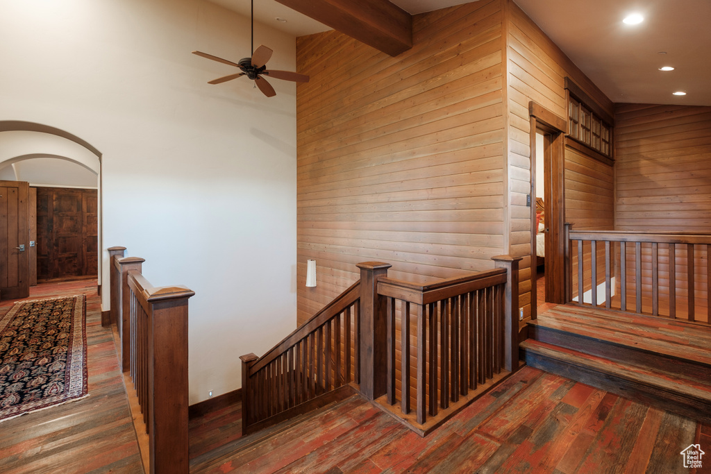 Stairs with wooden walls, wood-type flooring, recessed lighting, ceiling fan, and beam ceiling