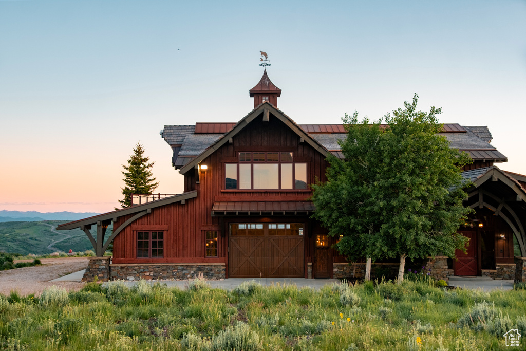 View of front of property featuring roof mounted solar panels, an attached garage, stone siding, and driveway